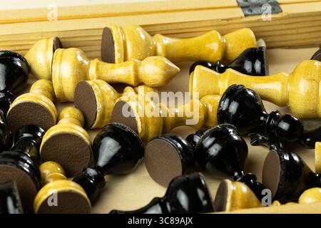 Eine Sammlung von Schachfiguren aus Holz in Schwarz-weiß-Farben, die in einer Holzkiste verstreut sind. Stockfoto