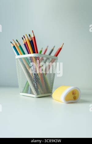 Weißer Schreibtisch mit Ständer mit farbigen Bleistiften und Skizzenbuch. Schulutensilien auf dem Tisch, wunderschön beleuchtet durch eine Schreibtischlampe Stockfoto