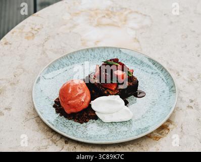 Dessertteller, schicke Platte, Schokoladenbrownie bedeckt mit frischen Erdbeeren und Minze, serviert mit Erdbeersorbet und Schlagsahne Stockfoto