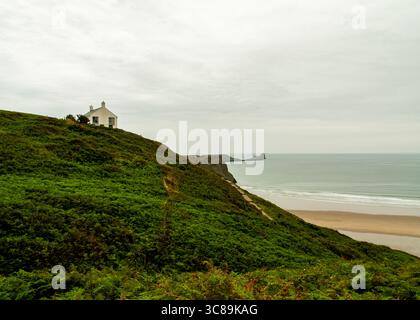 Ein weißes Haus liegt auf einem grünen Hügel mit Blick auf den Strand und das Meer. Stockfoto