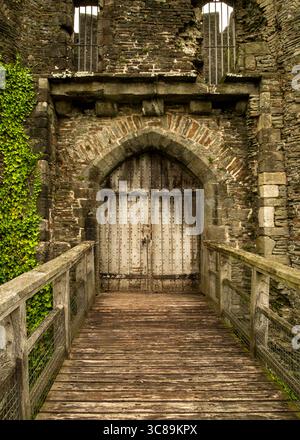 Eine Holzbrücke führt zu einer großen Holztür in einem Steinbogen. Die Tür ist mit Metallnieten versehen. Die Steinmauern sind verwittert und zeigen sig Stockfoto