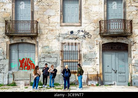 Gruppe junger Erwachsener vor dem verwitterten Steingebäude mit Graffiti in Porto, Portugal Stockfoto