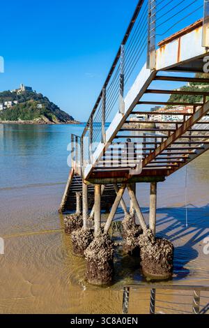 Die Metalltreppen führen hinunter zum Strand und zum Wasser, und eine Person geht die Treppe in der Ferne hoch. Befindet sich in San Sebastian, Spanien. Stockfoto