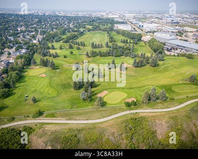 Golfplatz mit grünem Grasfeld und Pfad. Der Golfplatz ist von Bäumen und Häusern umgeben Stockfoto