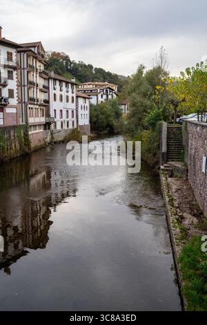 Malerischer Blick auf den Fluss Errobi, der an einem bewölkten Herbsttag durch das bezaubernde Dorf Saint-Jean-Pied-de-Port in Frankreich fließt. Stockfoto