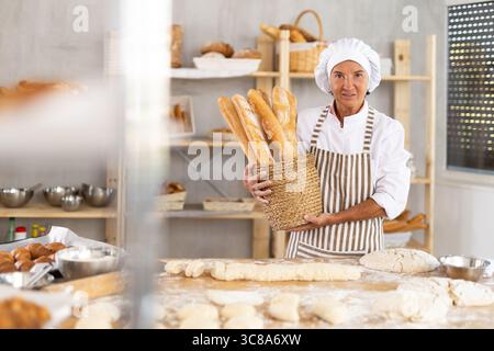 Porträt einer fröhlichen älteren Bäckerin mit Baguettes Stockfoto