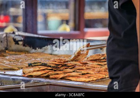 Ein Koch verwendet eine Zange, um frischen Fisch auf einer heißen Grillplatte zu grillen und ihn für ein beliebtes Fisch-Sandwich zu grillen, bei Ofne des Balik Sandwichbootes in Istanbul, Türkei Stockfoto
