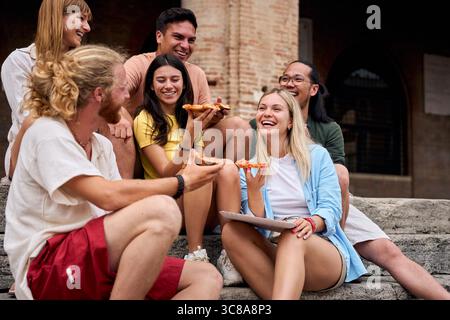 Glückliche Freunde essen Pizza im Freien, sitzen auf alten Steintreppen Stockfoto