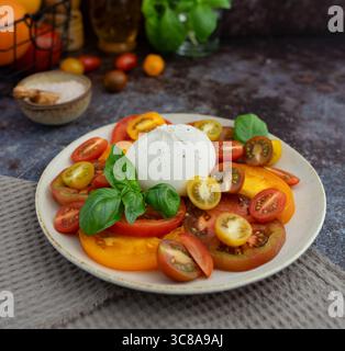 Nahaufnahme von Burrata mit geschnittenen Tomaten und Kirschtomaten, Basilikumblättern, Olivenöl und einer Schüssel Meersalz Stockfoto