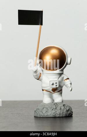 Nahaufnahme eines Astronautenspielzeugs über einem dunkelbraunen Holztisch mit schwarzer Flagge in der rechten Hand und weißem Hintergrund Stockfoto