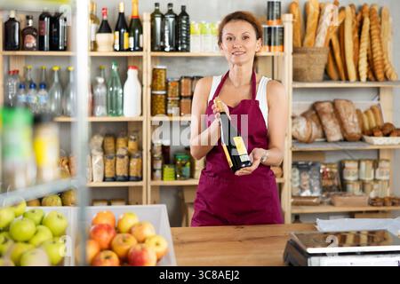 Die Verkäuferin für Erwachsene bietet Wein im Lebensmittelgeschäft an Stockfoto