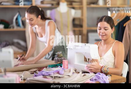 Der Modedesigner zeichnet neben einer Schneiderin Muster von Kleidern Stockfoto