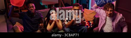 Gruppe multiethnischer junger Erwachsener, die auf dem Sofa sitzen und Sportereignisse beobachten, Schwarzer und Kaukasier, die Kissen heben, junge Frau und Mann, die mit Spannung und Vorfreude reagieren Stockfoto