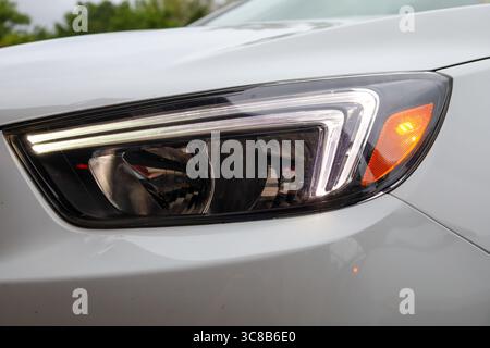 Eine Nahaufnahme des beleuchteten Scheinwerfers eines modernen weißen Autos. Stockfoto