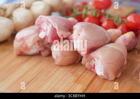 Frische Hähnchenschenkel und Kirschtomaten auf einem Schneidebrett Stockfoto