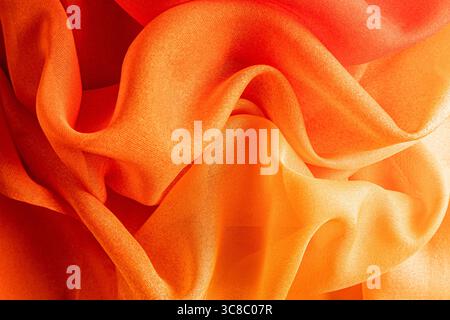 Kräftiges, leuchtendes Orange aus Seidenstoff. Weiche Wellen aus Seidenvorhängen in Herbstfarbe. Die Textur des Seidenstoffs ist in saftigen Rot- und Orangetönen gehalten. Stockfoto