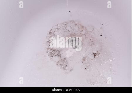 Im Waschbecken im Bad ist dreckiger Schaum und nach dem Waschen läuft das Wasser in die Kanalisation ab. Minimalistischer Blick auf das ablaufende Wasser in der weißen Wanne, das die tägliche hyg Stockfoto