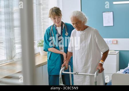 Ältere Frau, die Walker verwendet, unterstützt durch junge Erwachsene weibliche Gesundheitsberaterin Stockfoto