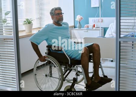 Birassischer Mann mittleren Alters mit Behinderung sitzend im Rollstuhl im Krankenhaus Stockfoto