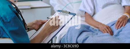 Frau, die im Krankenhausbett liegt, während die Schwester Notizen macht Stockfoto