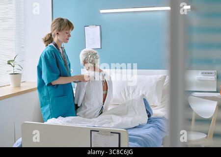 Junge kaukasische Ärztin untersucht ältere kaukasische Frau im Krankenhauszimmer Stockfoto