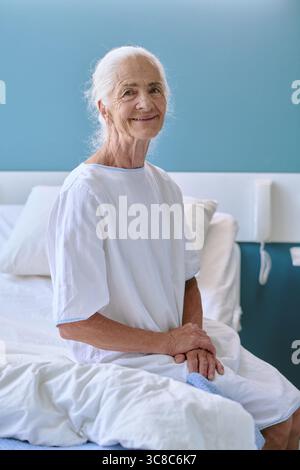 Porträt einer älteren kaukasischen Frau, die lächelnd auf dem Krankenhausbett sitzt Stockfoto