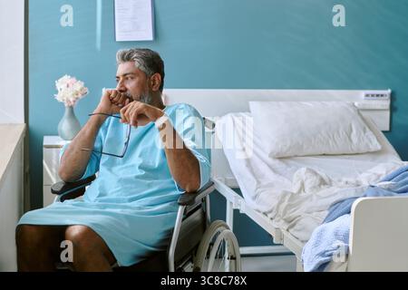 Birassischer Mann mittleren Alters mit Behinderung sitzend im Rollstuhl reflektierend Stockfoto