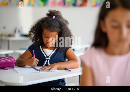 Fokussiertes Schulmädchen schreibt Notizen im Klassenzimmer. Stockfoto
