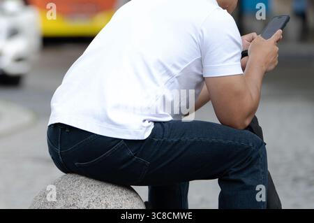 Stuttgart, Deutschland. August 2025. Ein Mann sitzt auf einem Steinpfosten und schaut sich sein Handy an. Quelle: Markus Lenhardt/dpa/Alamy Live News Stockfoto