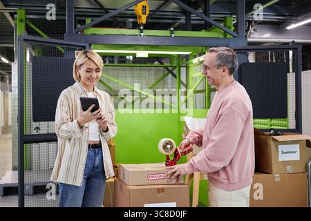 Kaukasischer Mann mittleren Alters, der der Frau Paketklebeband überreicht Stockfoto