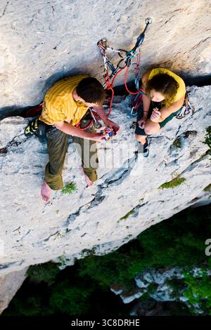 Ein männlicher und weiblicher Kletterer, der auf einem kleinen Felsvorsprung in der Verdon-Schlucht in Frankreich Essen teilt Stockfoto