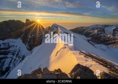 Aus der Vogelperspektive der Sonne, die goldenes Licht auf schneebedeckte Berggipfel wirft, bietet ein atemberaubendes Panorama, von oben gesehen, Location Unknown. Stockfoto