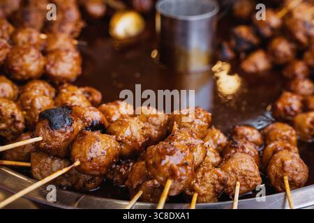 Beschreibungen:gegrillte Fleischbällchen auf Spießen, die in einer herzhaften Soße auf einem Street Food Market kochen. Stockfoto