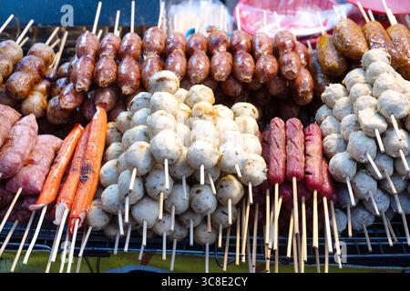 Eine Auswahl an gegrillten Schweinefleischwürsten einschließlich Sai Krok Isan und Moo Ping, Satay-Fleisch auf einem Stock, ein beliebtes thailändisches Straßenessen, das am Stand verkauft wird Stockfoto