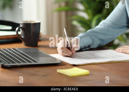 Nahaufnahme eines Mitarbeiters, der im Büro ein Arbeitsdokument auf einem Holztisch ausfüllt Stockfoto