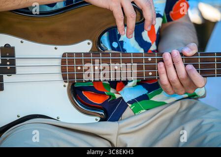 Hände spielen auf einer Bassgitarre mit einem weißen Pickguard. Elektrisches Instrument. Stockfoto