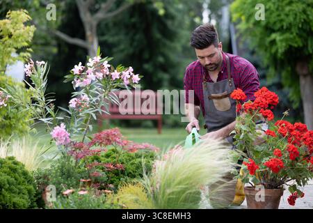 Der Mensch gießt vorsichtig Blumen in Töpfen, während er einen ruhigen Nachmittag in einem gepflegten Garten mit verschiedenen Pflanzen genießt Stockfoto