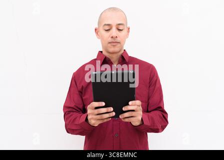 Reifer männlicher Profi in einem burgunderroten Button-Down-Shirt, das ein Tablet hält und verwendet. Isolierte Studioeinrichtung für Technik, Unternehmen oder Produktivität Stockfoto