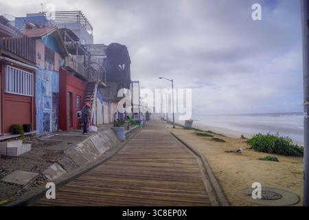 Blick auf die Promenade von Playas de Tijuana entlang der Pazifikküste in Mexiko mit farbenfrohen Häusern, einer einsamen Möwe und Wellen unter bewölktem Himmel. Stockfoto