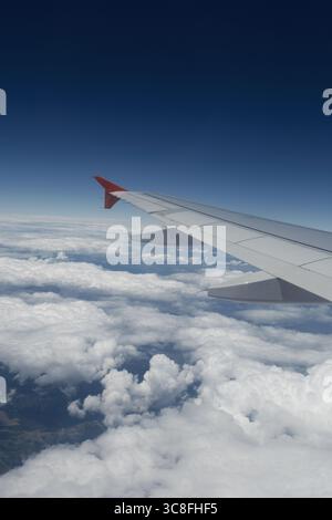 Ein ruhiger Blick auf einen Flugzeugflügel über dramatischen Wolken und Himmel, aufgenommen von einem Passagiersitz während des Fluges. Stockfoto