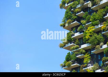 Lebendiger vertikaler Garten auf energieeffizientem Gebäude mit üppigem Grün auf Balkonen an der gesamten Fassade vor klarem blauem Himmel. Stockfoto