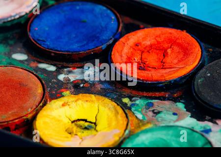 Nahaufnahme farbenfroher, rissiger und trockener Aquarellfarben in einer gut gebrauchten Palette, die die lebendigen Farben und die strukturierte Oberfläche zeigt Stockfoto