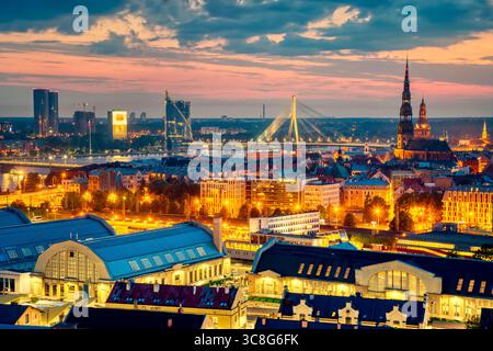 Wunderschönes Panorama von Riga Zentrum und Vansu Brücke über den Daugava Fluss während des atemberaubenden Sonnenuntergangs. Blick auf die beleuchtete Stadt Riga, die Hauptstadt von Lettland Stockfoto