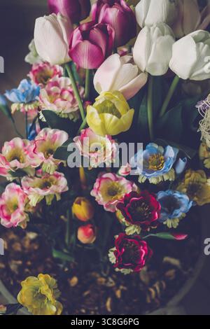 Künstliche Tulpen und andere bunte Blumen schaffen ein wunderschönes Blumenarrangement in einer Vase Stockfoto