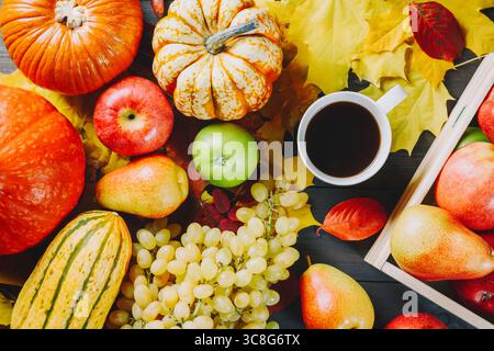 Reife Äpfel in einer Schachtel mit Kürbissen, Äpfeln, Trauben, Birnen und einer Tasse Kaffee auf dunklem hölzernem Hintergrund. Jahreszeitbild Herbst. Draufsicht. Stockfoto
