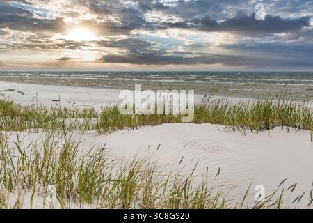 Weiße Sanddünen mit hohem Gras am Ostseestrand unter dramatischen Sonnenuntergangswolken Stockfoto