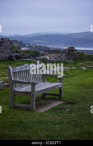 Eine verwitterte Parkbank aus Holz zwischen den Überresten der mittelalterlichen Burg von Aberystwyth in Wales an einem kalten und nebeligen Morgen. Stockfoto