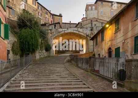 Blick auf das mittelalterliche Aquädukt von Perugia mit einer Steintreppe und einem Bogengang, der durch die engen Gassen der Stadt führt, beleuchtet Stockfoto
