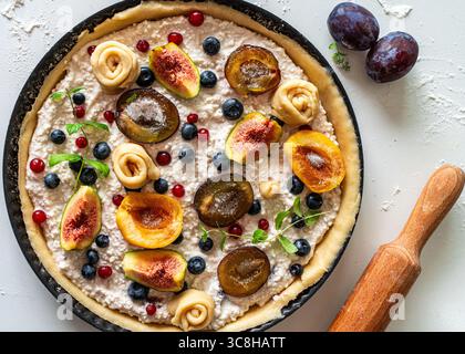 Eine Torte oder Hüttenkäsekuchen mit Früchten und Beeren in einer Form wird zum Backen vorbereitet und eine Nudelnadel auf einem hellen Hintergrund oder Tisch. Blick aus der ganzen Welt Stockfoto