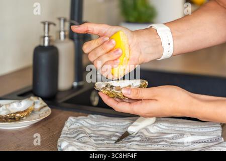 Frisch geöffnete Austern in der Hand gehalten und mit Zitronensaft bestreut. Hausgemachte Meeresfrüchte vor dem Essen Stockfoto